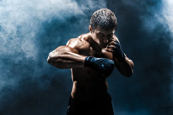 Muscular kickbox o muay thai luchador puñetazos en el humo . — Foto de Stock