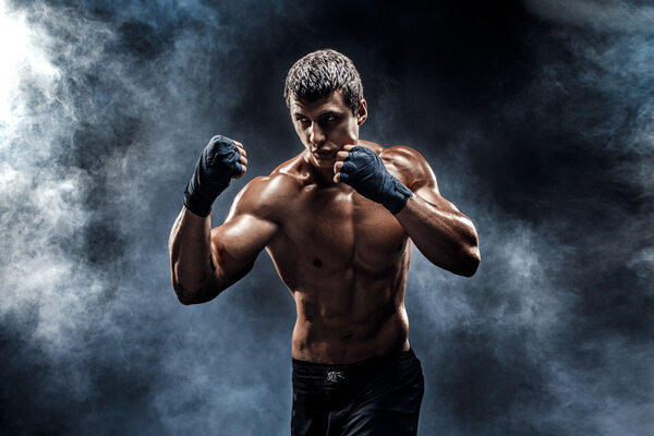 Muscular kick-box or muay thai fighter punching in smoke.