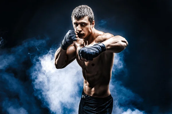 Muscular kick-box or muay thai fighter punching in smoke. — Stock Photo, Image