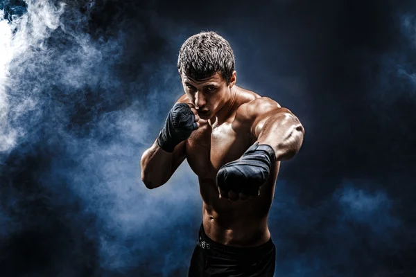 Muscular kick-box or muay thai fighter punching in smoke.