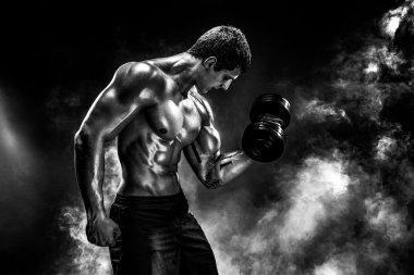 Konsantre olmuş kaslı adam dambılla egzersiz yapıyor.