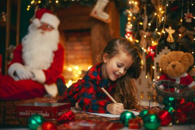 Mutlu Noeller, tatlı küçük kız Noel Baba arka planda uyurken ona mektup yazıyor.