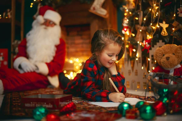 Joyeux Noël, petite fille mignonne écrit la lettre au Père Noël, alors qu'il dort sur le fond — Photo