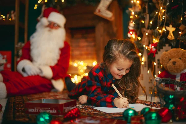 Щасливого Різдва, маленька дівчинка-Мила пише листа Санті Клаусу, коли він спить на задньому плані. — стокове фото