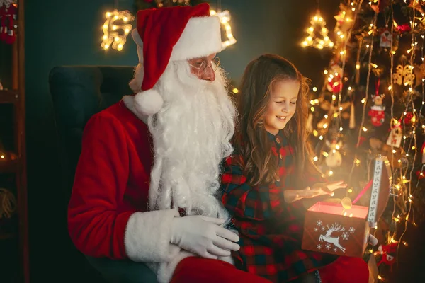 Санта Клаус з милою дівчиною відкриває в кімнаті магічну коробку з подарунками. Різдво — стокове фото