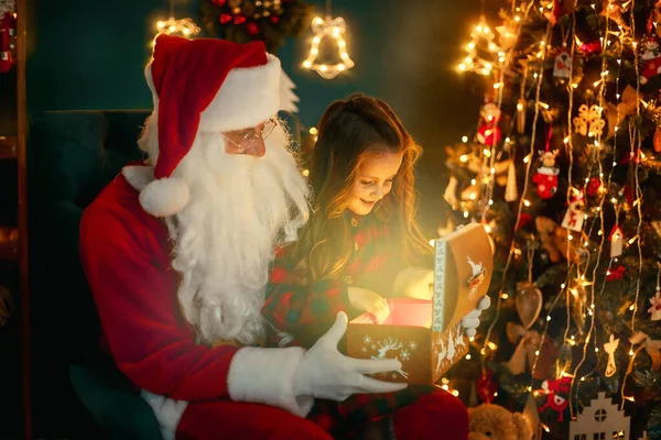 Jultomten med en liten söt flicka öppna magiska presentförpackning i rummet. Juletid — Stockfoto