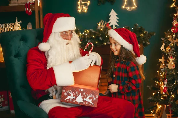 Санта Клаус з милою дівчиною відкриває в кімнаті магічну коробку з подарунками і купує цукерки. Різдво — стокове фото