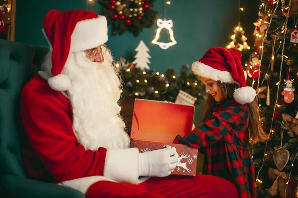 Санта Клаус з милою дівчиною відкриває в кімнаті магічну коробку з подарунками. Різдво — стокове фото