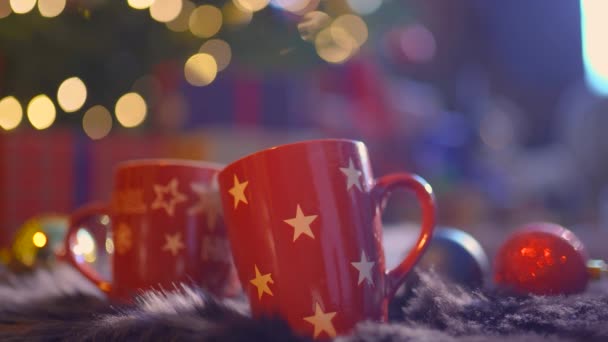 Close-up zwei Glasbecher voller heißer, roter, aromatischer Getränke mit verschwommenem weihnachtlichem Hintergrund — Stockvideo