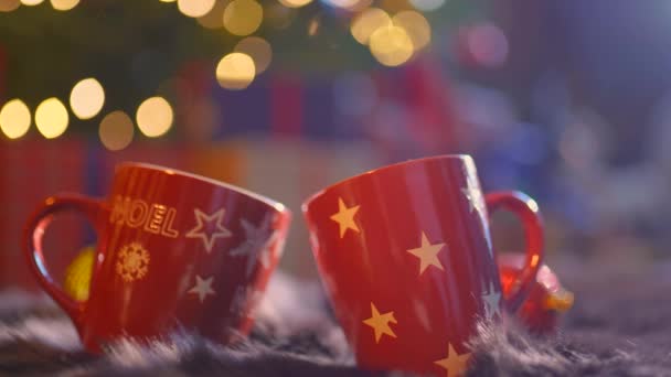 Zamknij dwa szklane kubki pełne gorącego, czerwonego, aromatycznego napoju z rozmytym tłem świątecznym — Wideo stockowe