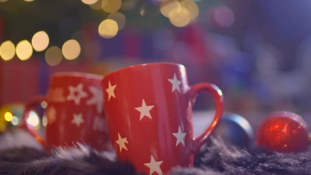 Gros plan deux tasses en verre pleines de boisson chaude, rouge et aromatique avec fond de Noël flou — Video