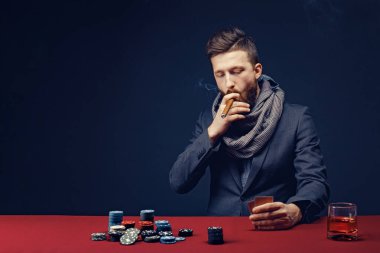 Siyah kumarhanede oynayan, puro içen, viski içen şık sakallı adam.