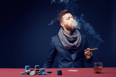 Siyah kumarhanede oynayan, puro içen, viski içen şık sakallı adam.
