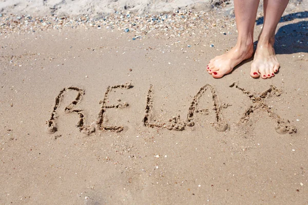 Escrito a mano Relajarse Palabra en la costa de arena. Maravillosas palabras en arena de playa. Concepto de idea de amor — Foto de Stock