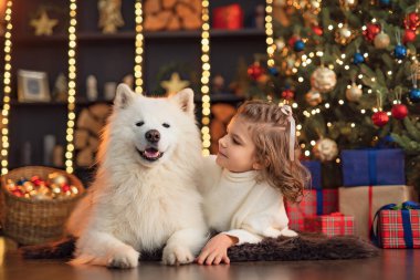 Noel ağacının yanında beyaz bir köpekle küçük tatlı bir kız.