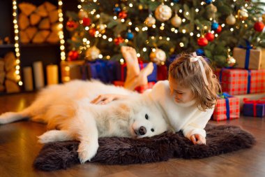 Noel ağacının yanında beyaz bir köpekle küçük tatlı bir kız.