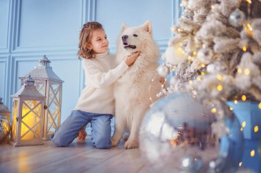 Noel ağacının yanında beyaz bir köpekle küçük tatlı bir kız.