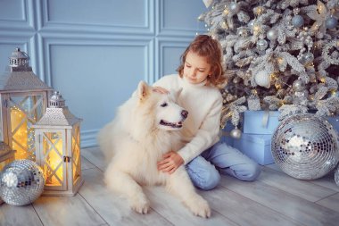Noel ağacının yanında beyaz bir köpekle küçük tatlı bir kız.
