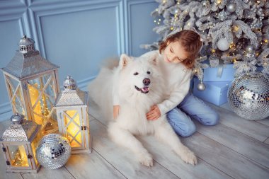 Noel ağacının yanında beyaz bir köpekle küçük tatlı bir kız.