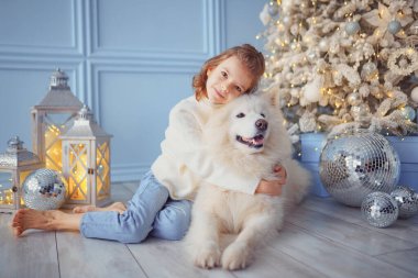 Noel ağacının yanında beyaz bir köpekle küçük tatlı bir kız.