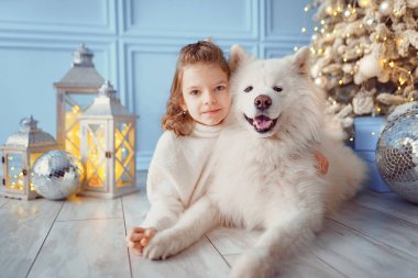 Noel ağacının yanında beyaz bir köpekle küçük tatlı bir kız.