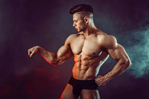 Athletischer Mann, der im Studio vor dunklem Hintergrund mit Rauch die Muskeln spielen lässt. Starker Bodybuilder mit perfektem Bauch — Stockfoto