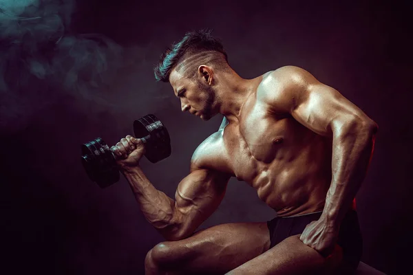 Sportowiec napinający mięśnie w studio na ciemnym tle dymem. Silny kulturysta z doskonałym brzuchem — Zdjęcie stockowe