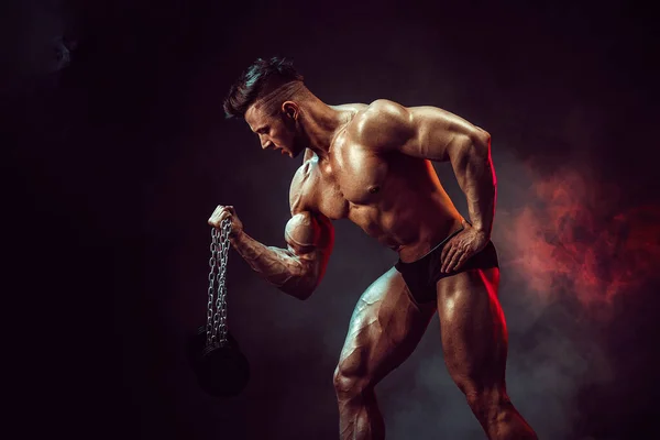 Atlétikai férfi hajlító izmok stúdió sötét háttérrel füst. Erős testépítő tökéletes hasizmokkal — Stock Fotó