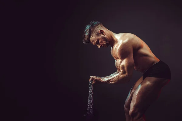 Hombre atlético flexionando los músculos en el estudio sobre fondo oscuro con humo. Culturista fuerte con abdominales perfectos — Foto de Stock