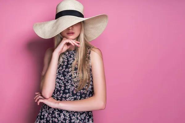Foto de belleza de la atractiva mujer sensual con sombrero de ala de paja, posando sobre fondo de estudio rosa —  Fotos de Stock