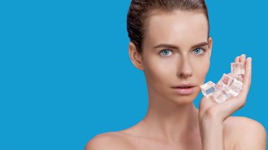 Güzel kadın mavi arka planda buz küpü tedavisi uyguluyor.