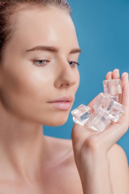 Güzel kadın mavi arka planda buz küpü tedavisi uyguluyor.