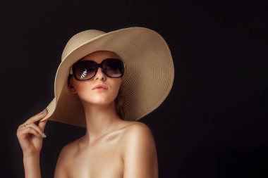 Stüdyonun arka planında saman kenarlı şapka ve büyük güneş gözlüğü takan çekici, şehvetli bir kadının güzel fotoğrafı.