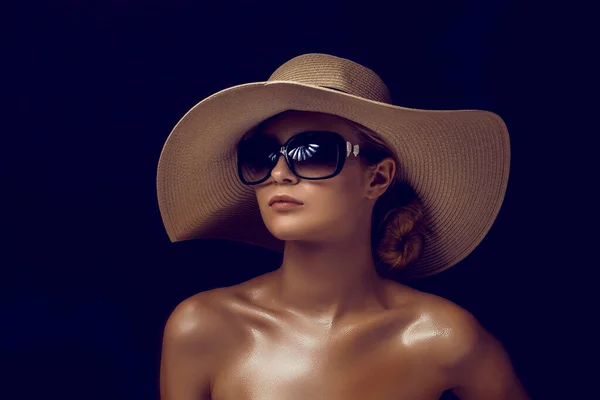 Foto kecantikan wanita sensual yang menarik mengenakan topi berjerami dan kacamata hitam besar yang berpose di latar belakang studio gelap — Stok Foto
