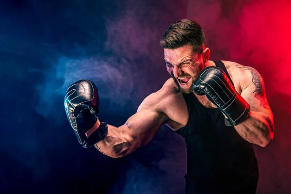 Barbudo tatuado desportista muay thai boxer em camiseta preta e luvas de boxe lutando no fundo escuro com fumaça. — Fotografia de Stock