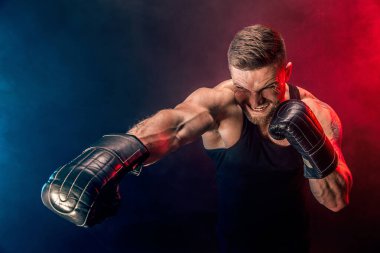 Sakallı sporcu Muay Thai boksörü siyah fanilalı ve boks eldivenli siyah arka planda dumanla dövüşüyor..