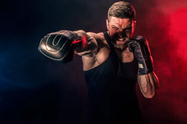 Barbudo deportista tatuado muay thai boxeador en camiseta negra y guantes de boxeo luchando sobre fondo oscuro con humo. — Foto de Stock