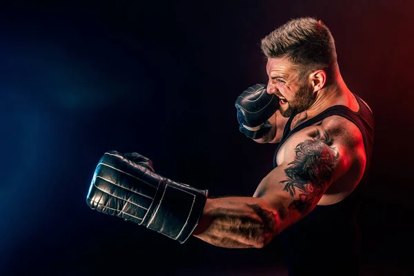 Barbudo deportista tatuado muay thai boxeador en camiseta negra y guantes de boxeo luchando sobre fondo oscuro con humo. —  Fotos de Stock