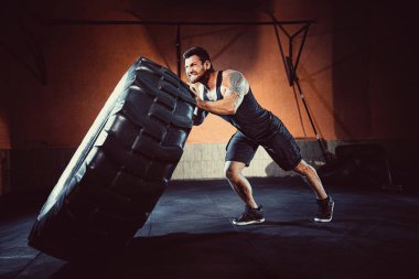 Vücut geliştirme eğitimi, sakallı güçlü sporcu, kaslı vücut, spor salonunda ağır tekerlekleri kaldırıyor.
