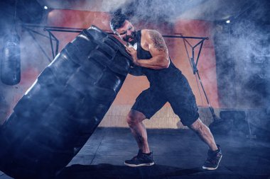 Vücut geliştirme eğitimi, sakallı güçlü sporcu, kaslı vücut, spor salonunda ağır tekerlekleri kaldırıyor.