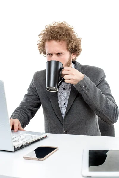 Gekruld zakenman met beker in de hand werken op laptop — Stockfoto