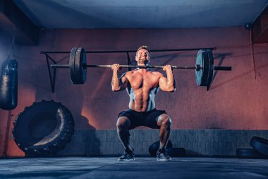 Modern fitness merkezinde kaslı fitness adamı halterle kafasına vuruyor. İşlevsel eğitim. Kapma egzersizi.