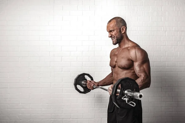 Bodybuilder doing exercises for biceps with a barbell against brick wall — Stock Photo, Image