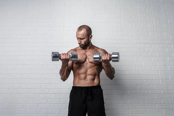 Bodybuilder macht Übungen für Bizeps mit Kurzhanteln gegen Ziegelwand — Stockfoto