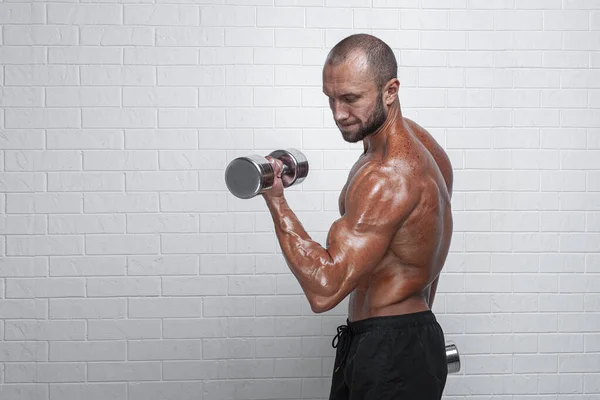Culturista haciendo ejercicios para bíceps con mancuernas contra pared de ladrillo — Foto de Stock