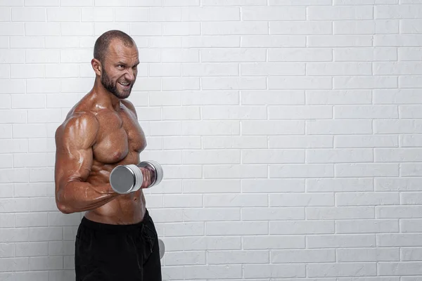 Bodybuilder gör övningar för biceps med hantlar mot tegelvägg — Stockfoto