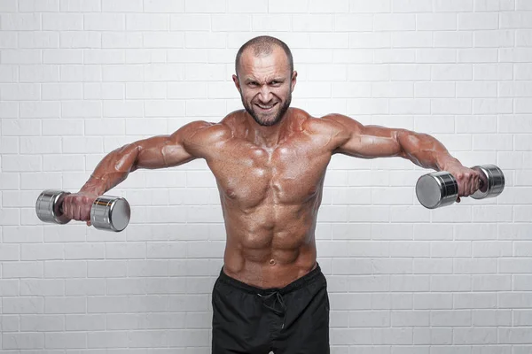 Bodybuilder doet oefeningen voor deltaspier spieren met een halters tegen bakstenen muur — Stockfoto