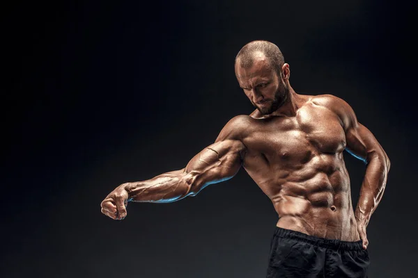 Hombre fuerte con abdominales, hombros, bíceps, tríceps y pecho perfectos. Culturista en topless flexionando sus músculos sobre fondo negro — Foto de Stock