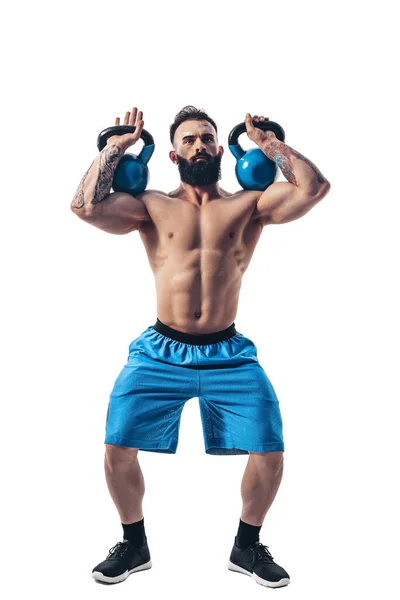 Muskulös skjorta tatuerade skäggiga manliga idrottare bodybuilder träning med kettlebell på en vit bakgrund. — Stockfoto