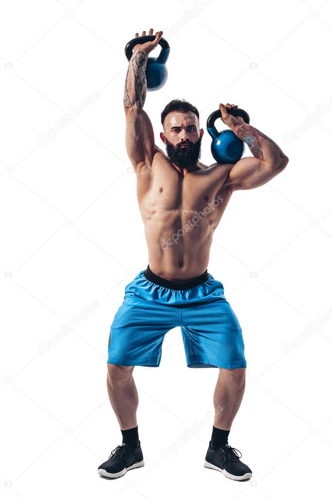 Muscular shirtless tattooed bearded male athlete bodybuilder workout with kettlebell on a white background.